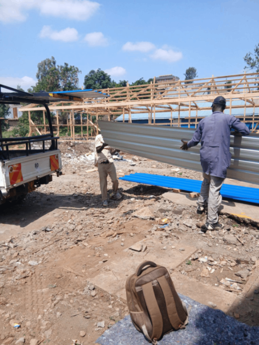 Grey corrugated mabati delivered to a construction site with timber roof trusses ready for installation