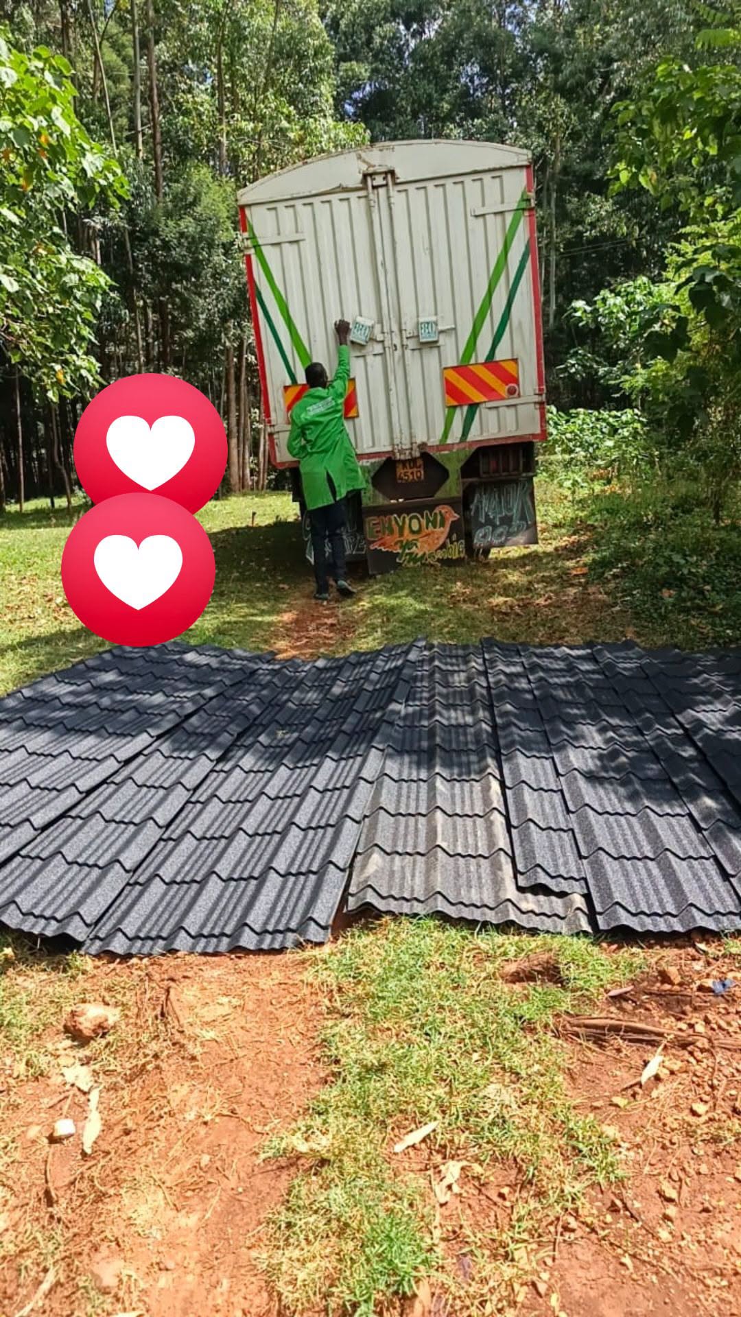 Black stone-coated roofing tiles offloaded next to a delivery lorry at a rural homestead